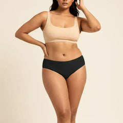 Woman wearing a beige sports bra and black low-waist bikini on a beige background