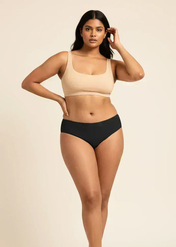 Woman wearing a beige sports bra and black low-waist bikini on a beige background