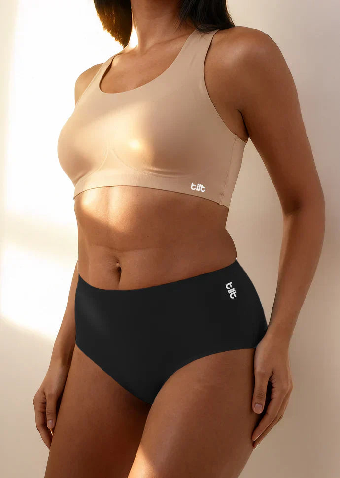 Person wearing a beige sports bra and black mid-waist underwear with 'tilt' branding.