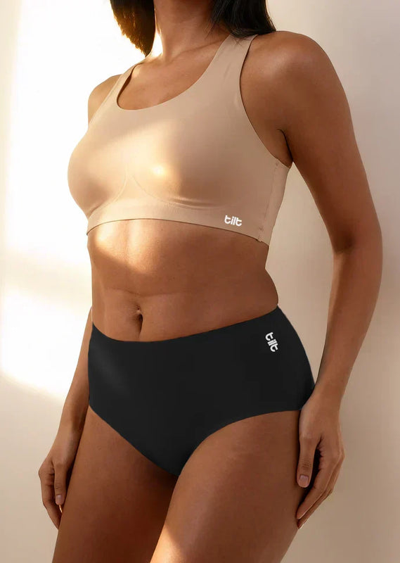 Person wearing a beige sports bra and black mid-waist underwear with 'tilt' branding.