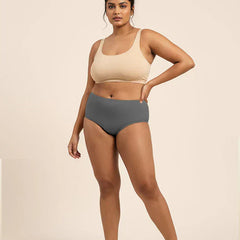 Woman wearing a beige sports bra and gray mid-waist underwear on a beige background