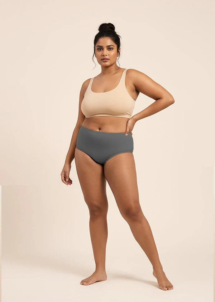 Woman wearing a beige sports bra and gray mid-waist underwear on a beige background