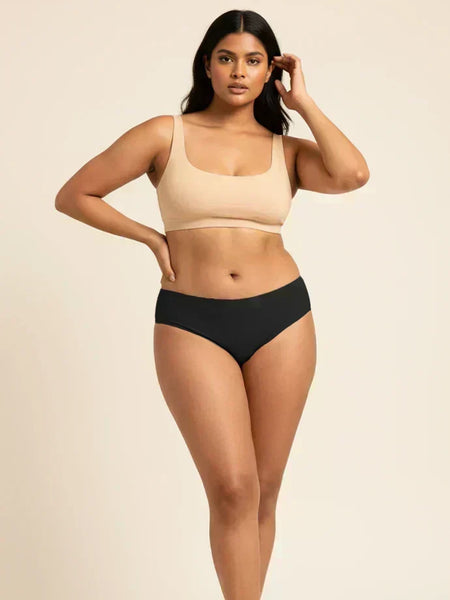 Woman wearing a beige sports bra and black low-waist bikini on a beige background