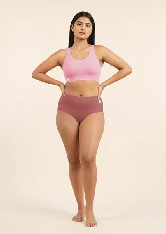 Woman wearing a pink sports bra and  pink mid-waist underwear on a beige background