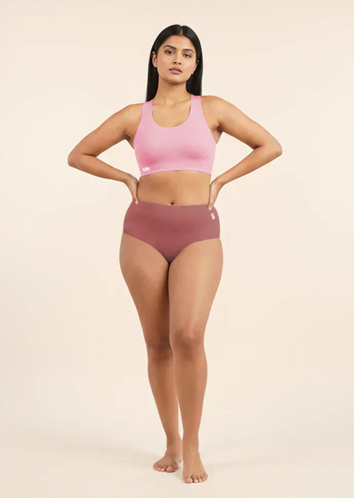 Woman wearing a pink sports bra and  pink mid-waist underwear on a beige background