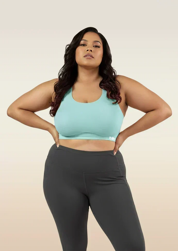 Woman wearing a blue sports bra and dark gray leggings on a beige background