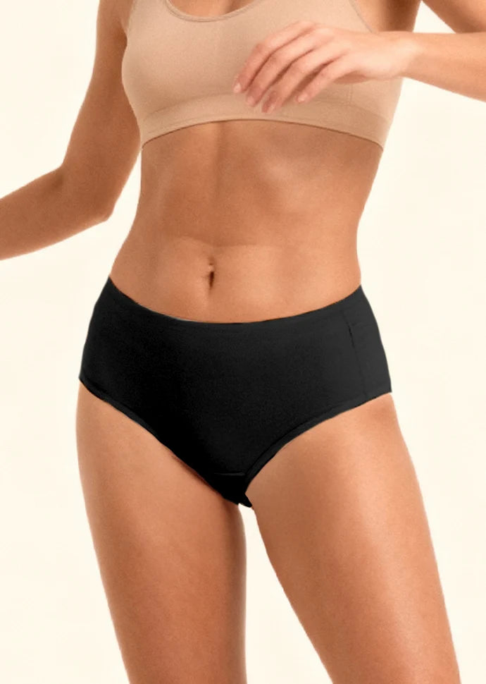 Person wearing black mid-waisted underwear and beige sports bra on a plain background