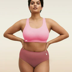 Woman wearing a pink sports bra and mid-waist pink underwear on a beige background