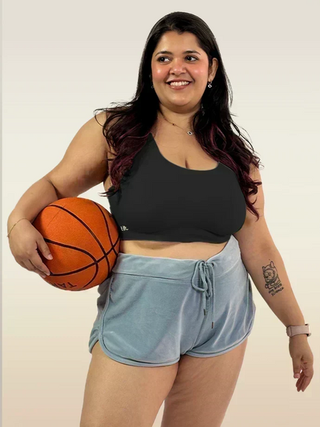 Woman holding a basketball wearing a black sports bra and light blue shorts on a plain background