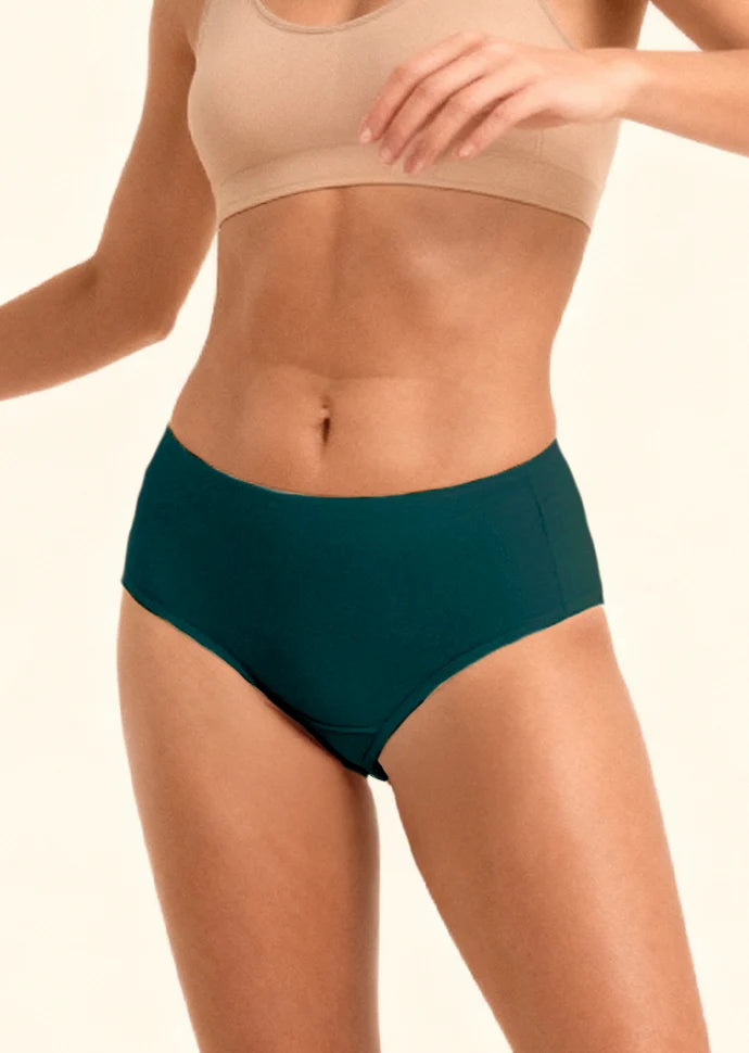 Person wearing teal mid-waist  underwear and beige sports bra on a plain background