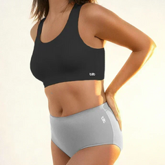 Woman wearing a black sports bra and gray mid-waist brief in warm sunlight