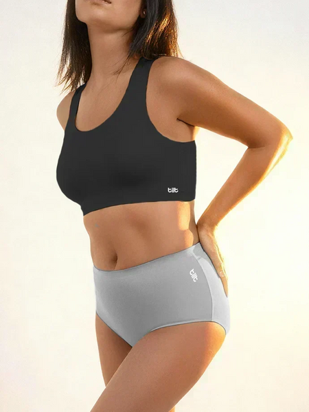 Woman wearing a black sports bra and gray mid-waist brief in warm sunlight