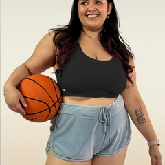 Woman holding a basketball wearing a black sports bra and light blue shorts on a plain background