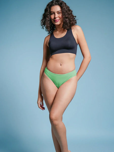 Woman wearing a black sports bra and green bikini bottoms on a blue background