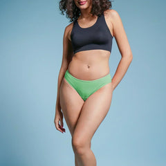 Woman wearing a black sports bra and green bikini bottoms on a blue background