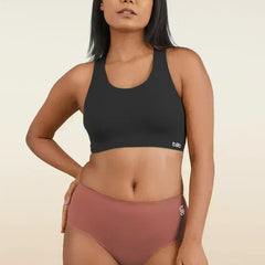 Woman wearing a black sports bra and rose gold mid-waist underwear on a beige background