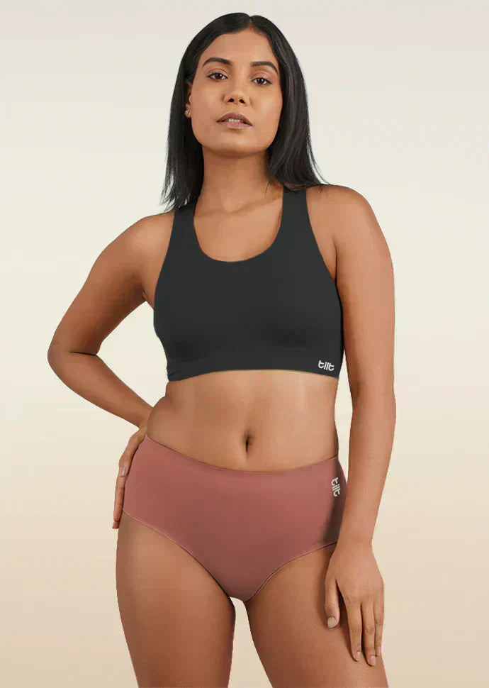 Woman wearing a black sports bra and rose gold mid-waist underwear on a beige background