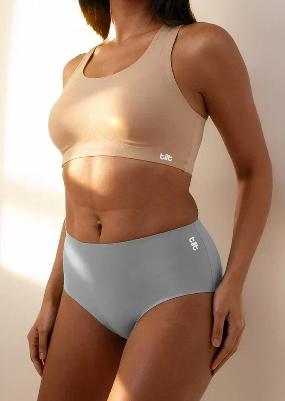 Person wearing a beige sports bra and grey mid-waist underwear with 'tilt' branding