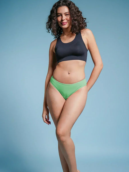 Woman wearing a black sports bra and green bikini bottoms on a blue background