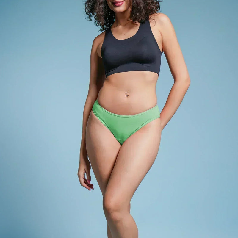 Woman wearing a black sports bra and green bikini bottoms on a blue background