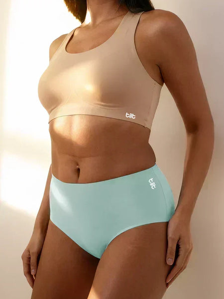A person wearing a beige sports bra and blue mid-waist briefs with a white 
