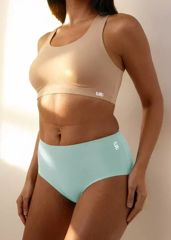 A person wearing a beige sports bra and blue mid-waist briefs with a white 