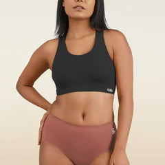 Woman wearing a black sports bra and rose gold mid-waist underwear on a beige background