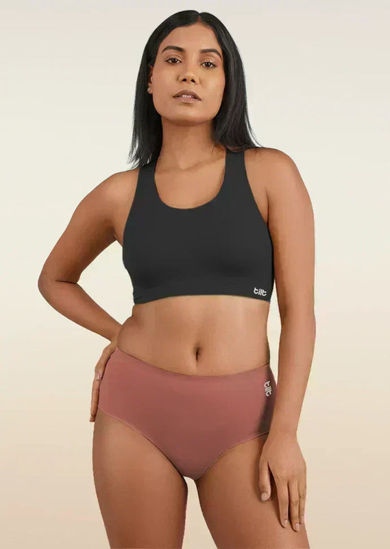 Woman wearing a black sports bra and rose gold mid-waist underwear on a beige background