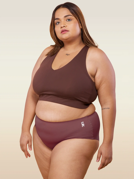 Woman wearing a brown bra and pink underwear on a beige background