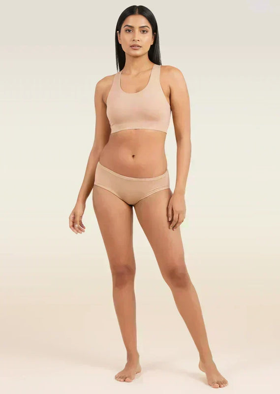 Woman wearing a beige sports bra and low-waist underwear on a plain background