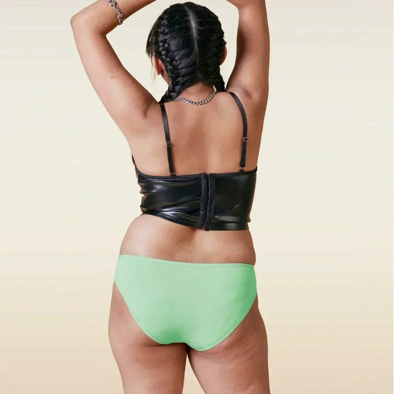 Person wearing a black leather top and green bikini underwear on a beige background