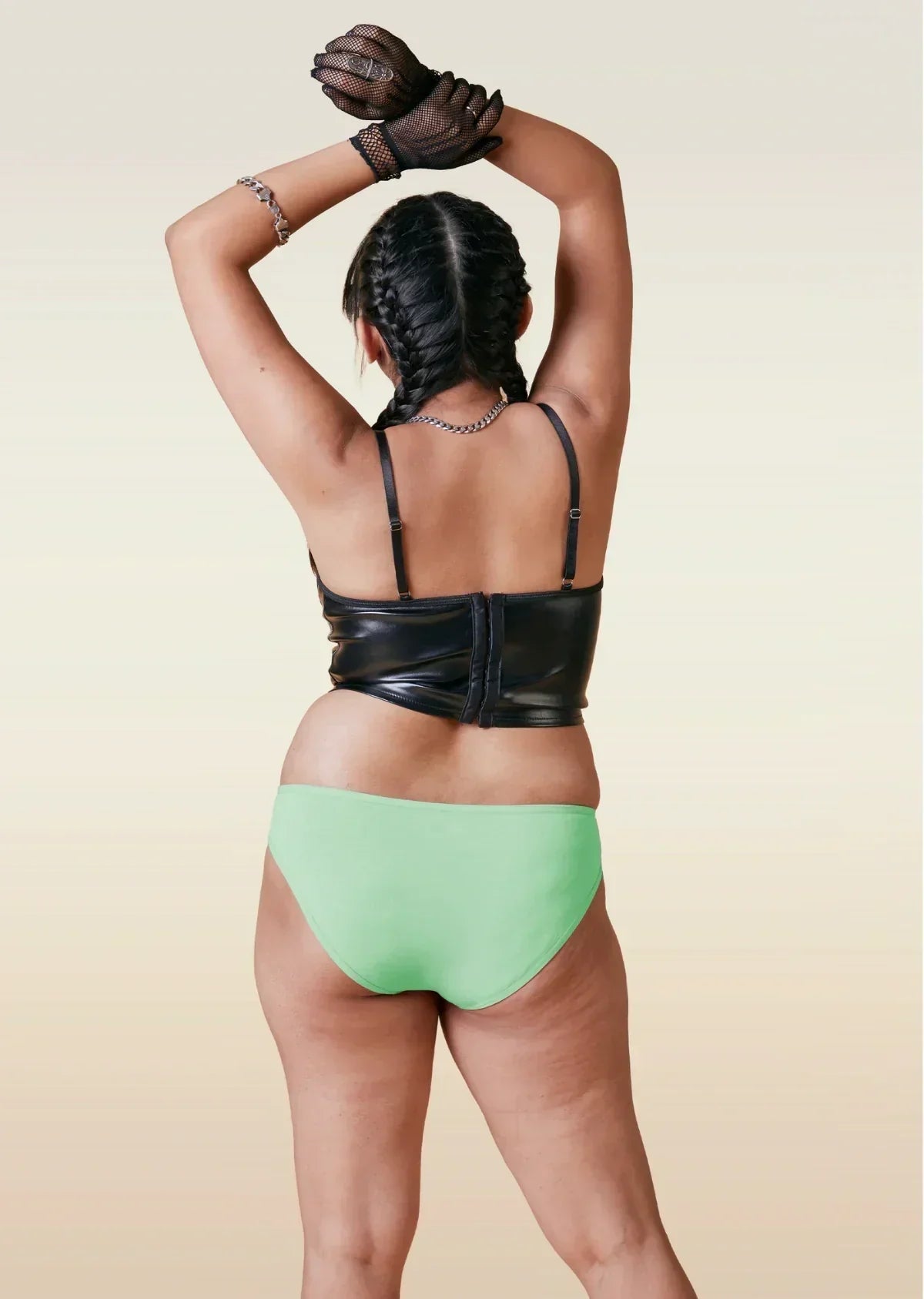 Person wearing a black leather top and green bikini underwear on a beige background