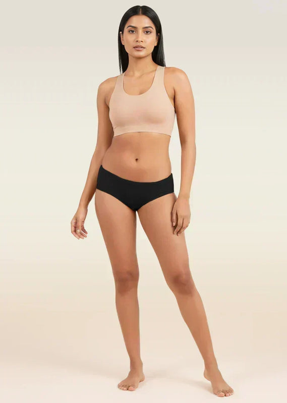 Woman wearing a beige sports bra and black low-waist underwear on a plain background