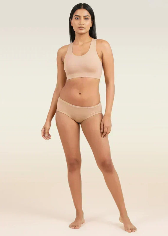 Woman wearing a beige sports bra and low-waist underwear on a plain background