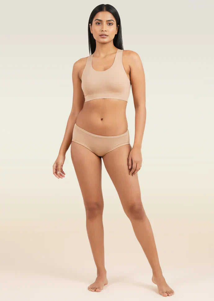 Woman wearing a beige sports bra and low-waist underwear on a plain background