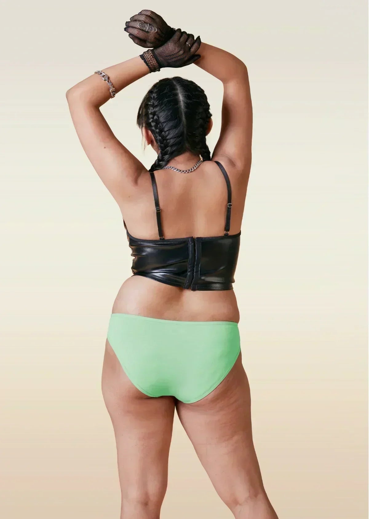 Person wearing a black leather top and green bikini underwear on a beige background