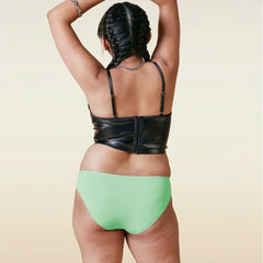 Person wearing a black leather top and green bikini underwear on a beige background