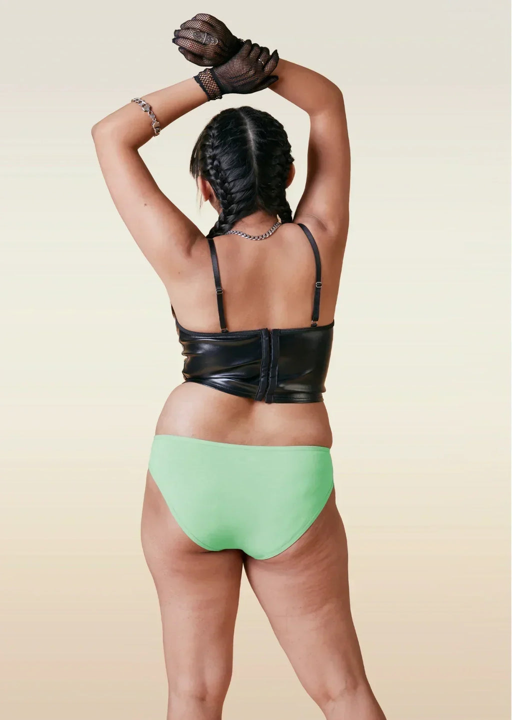 Person wearing a black leather top and green bikini underwear on a beige background