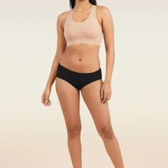 Woman wearing a beige sports bra and black low-waist underwear on a plain background