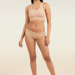 Woman wearing a beige sports bra and low-waist underwear on a plain background