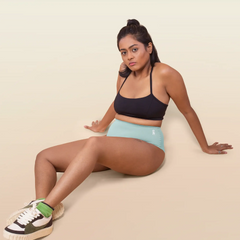 Woman sitting on a beige surface wearing a black sports bra and blue underwear.