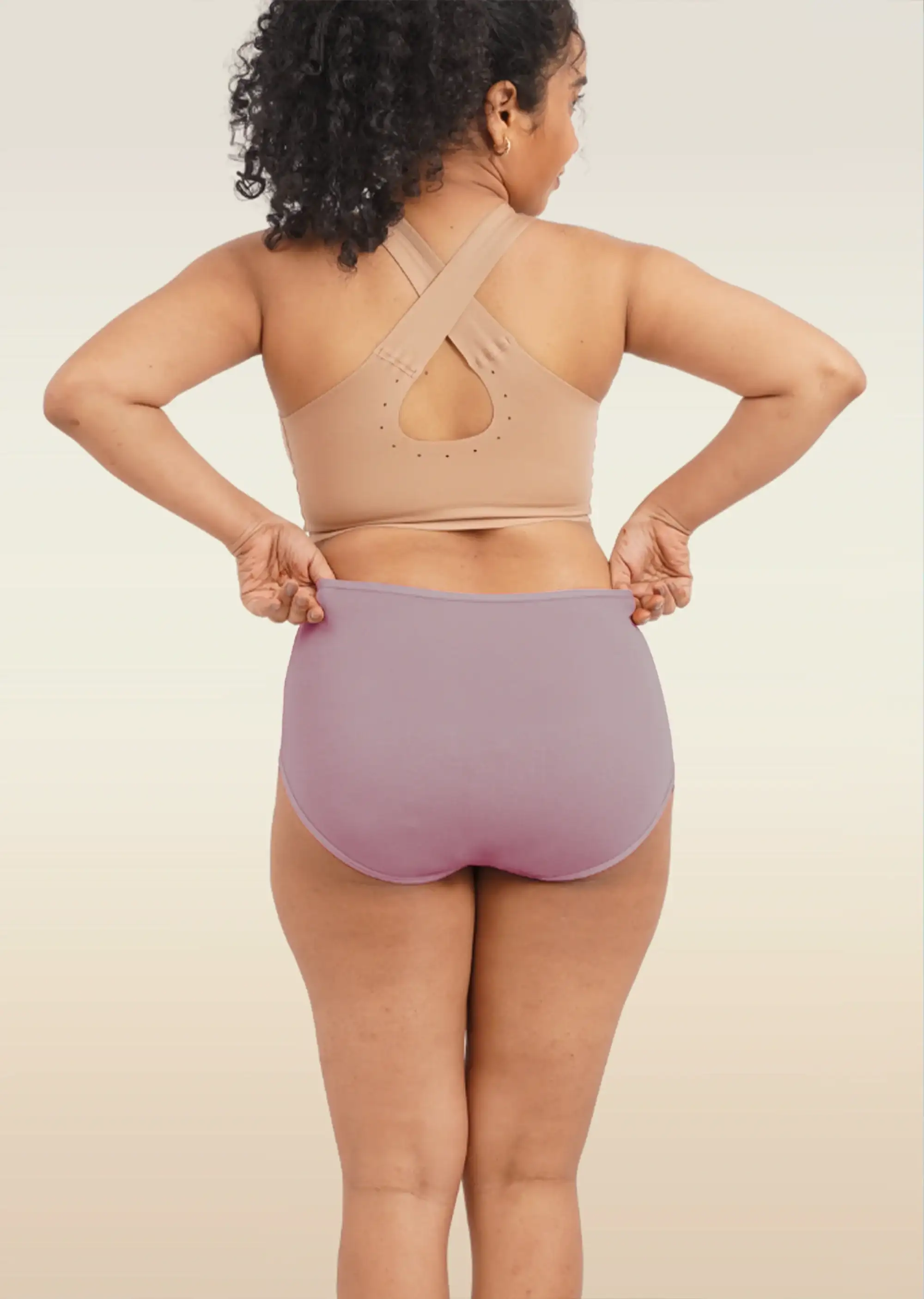 Person wearing a beige sports bra and brown high-waisted underwear on a plain background