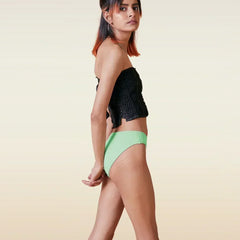Woman wearing a black top and green  bikini underwear on a beige background