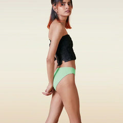Woman wearing a black top and green  bikini underwear on a beige background