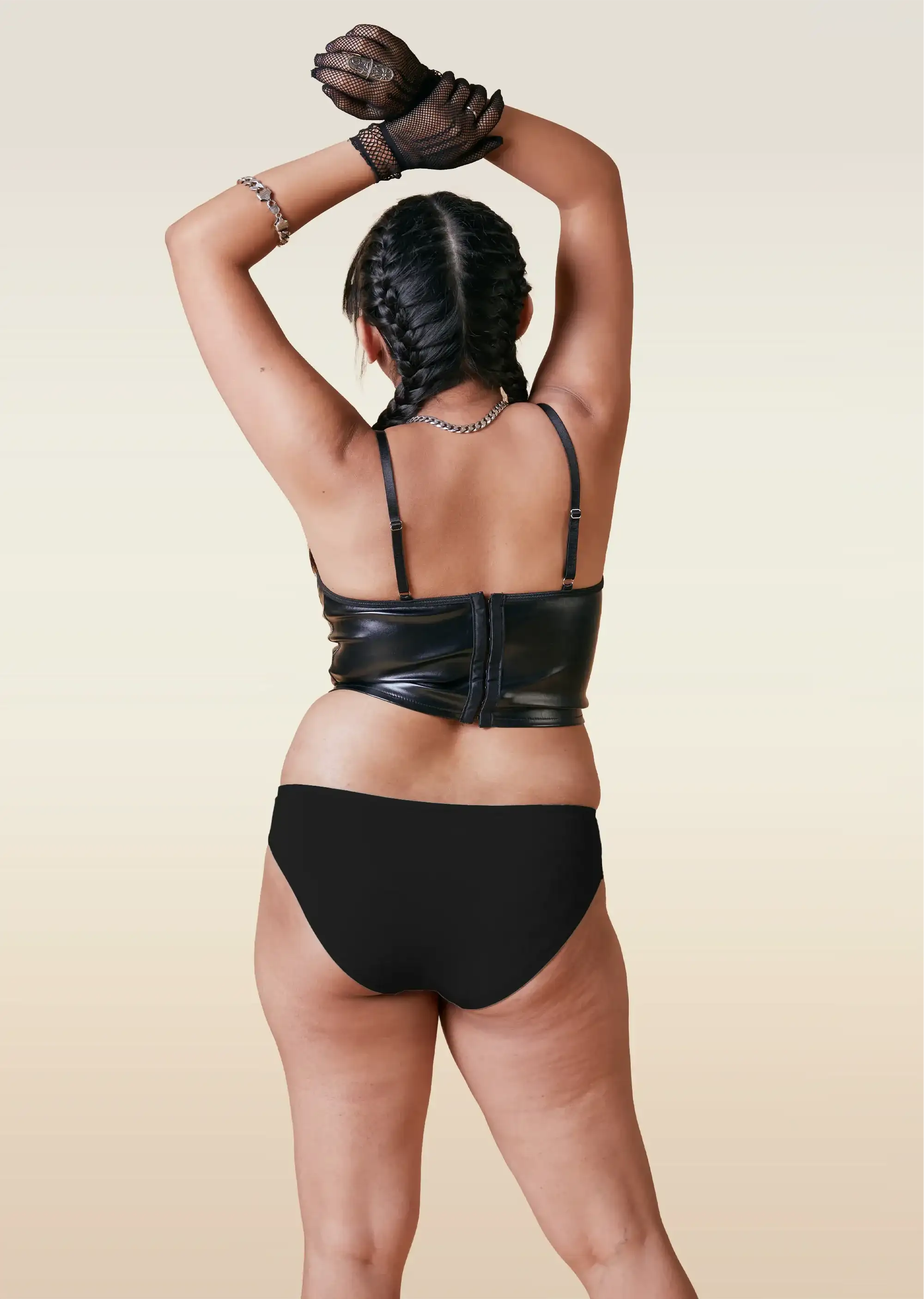 Person wearing a black leather outfit and black underwear with gloves on a beige background