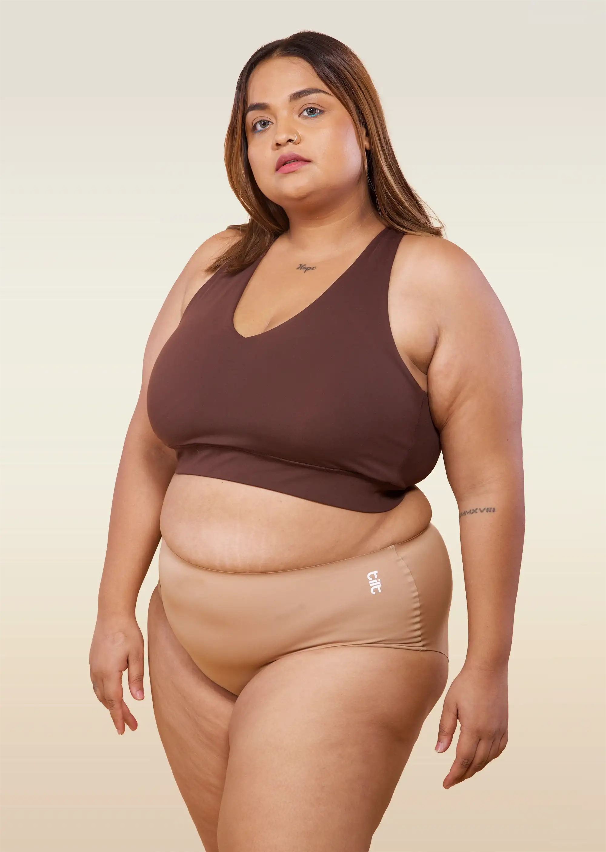 Woman wearing a brown sports bra and beige mid-waist underwear on a beige background