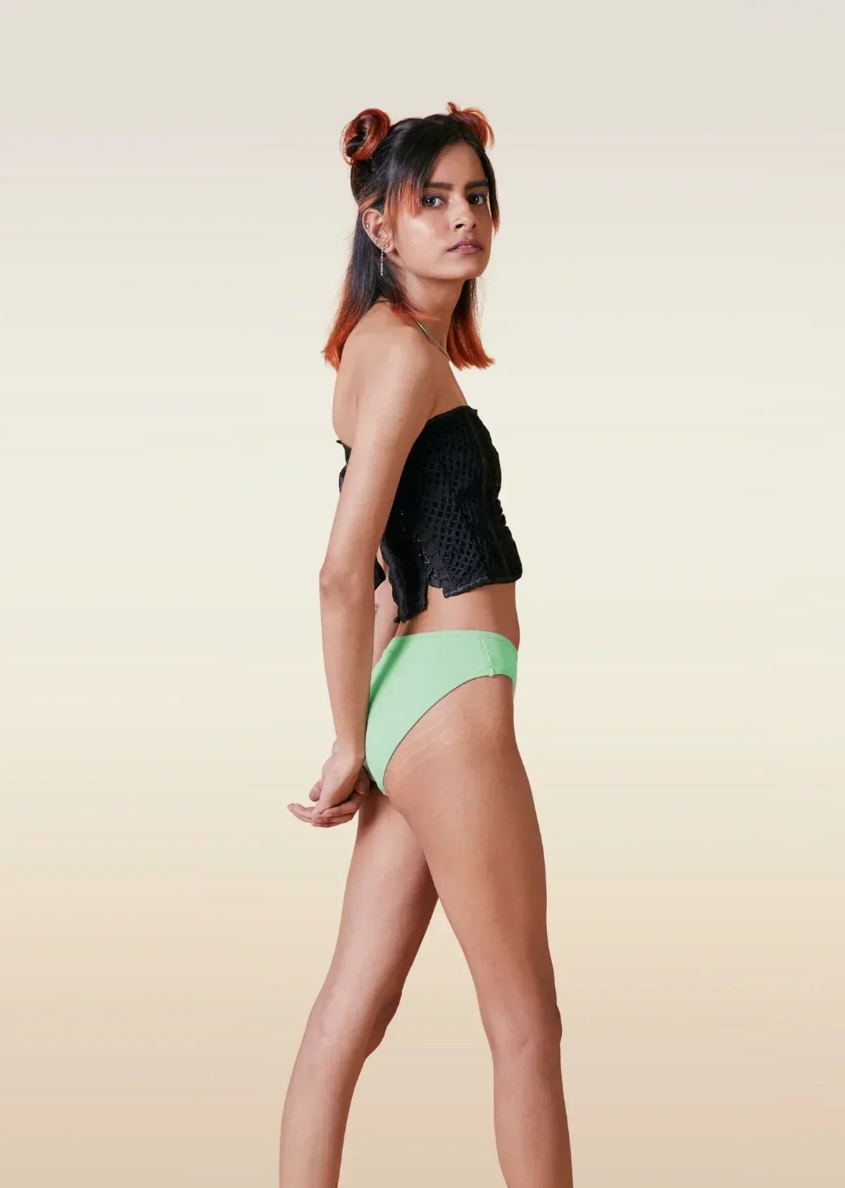 Woman wearing a black top and green bikini bottoms on a beige background