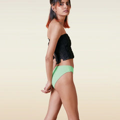 Woman wearing a black top and green bikini bottoms on a beige background
