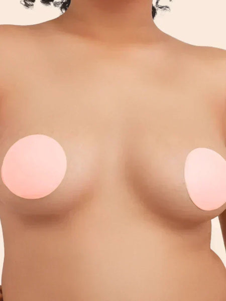 Close-up of a person wearing round, beige nipple covers against a plain background.