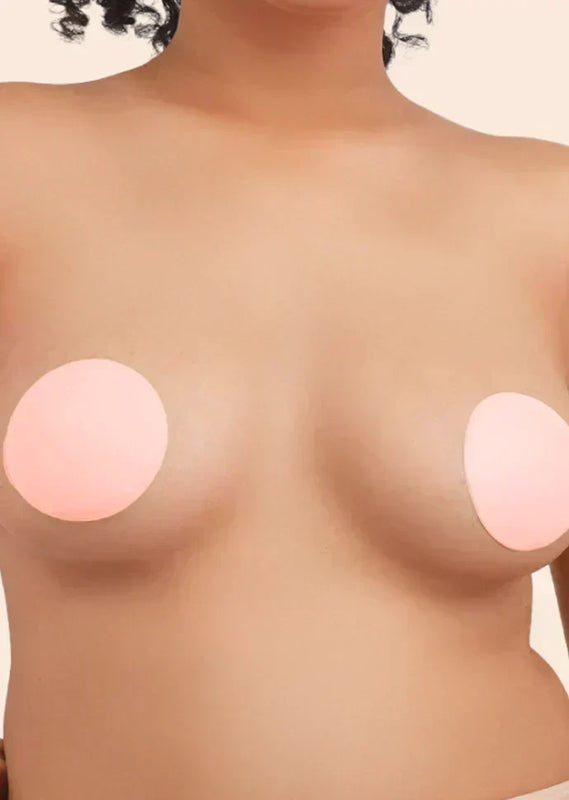 Close-up of a person wearing round, beige nipple covers against a plain background.
